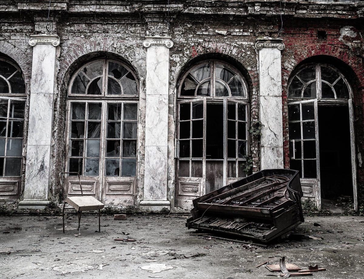 A crumbled grand piano in front of a ruined building.